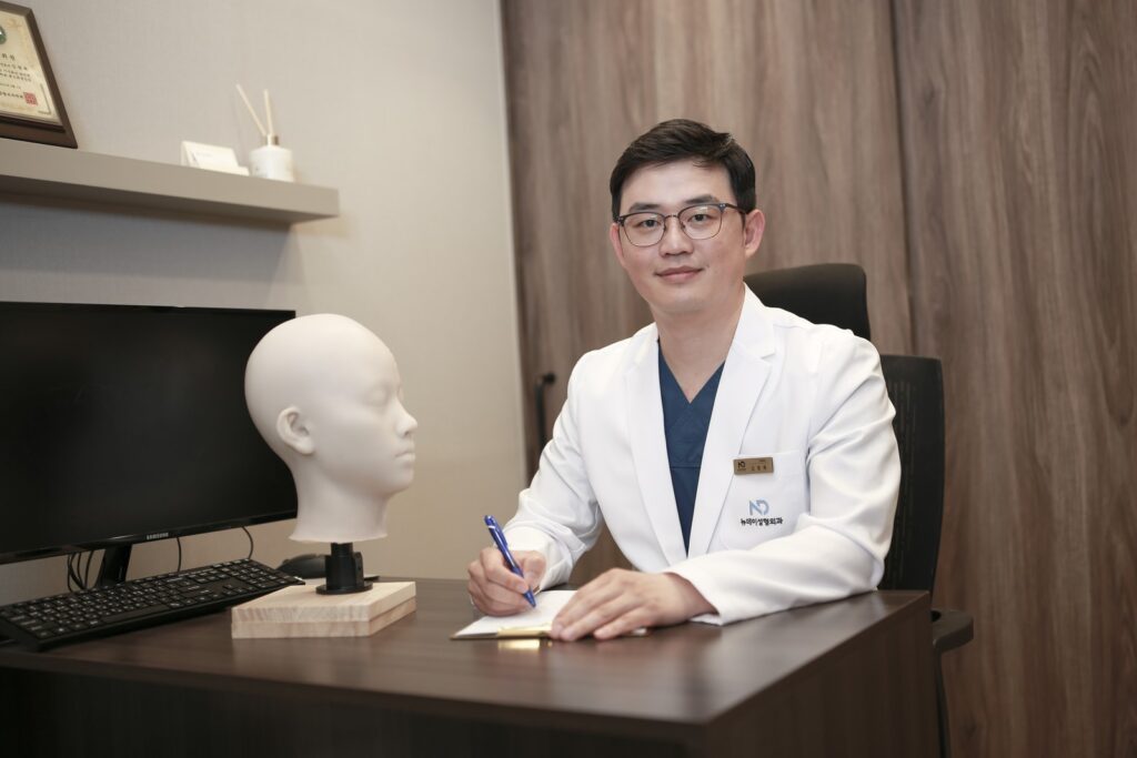 논현역 뉴데이성형외과 원장이 진료실 책상에서 펜을 들고 있는 모습